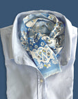 Ottimare frilly dames sjaal met jasmijnen in hemels blauw en geel. Handgemaakt in Nederland van duurzame kunst zijde met twill weving. De sjaal is duo-face met twee kanten en heeft een franje en staat mooi op een lichtblauw overhemd.