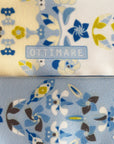 Detail van Ottimare twilly dames sjaal met jasmijn bloemen in hemelsblauw en geel met logo in blauw. Het sjaaltje is handgemaakt van dubbele duurzame eco twill kunst zijde in Nederland.