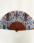 Elegante waaier van Ottimare met print op duurzame kunst zijde met Thangka dansers in donker blauw en sienna oranje. Het frame is van Kotibé hout en handgemaakt in Spanje. De waaier heeft een goudkleurige ring.