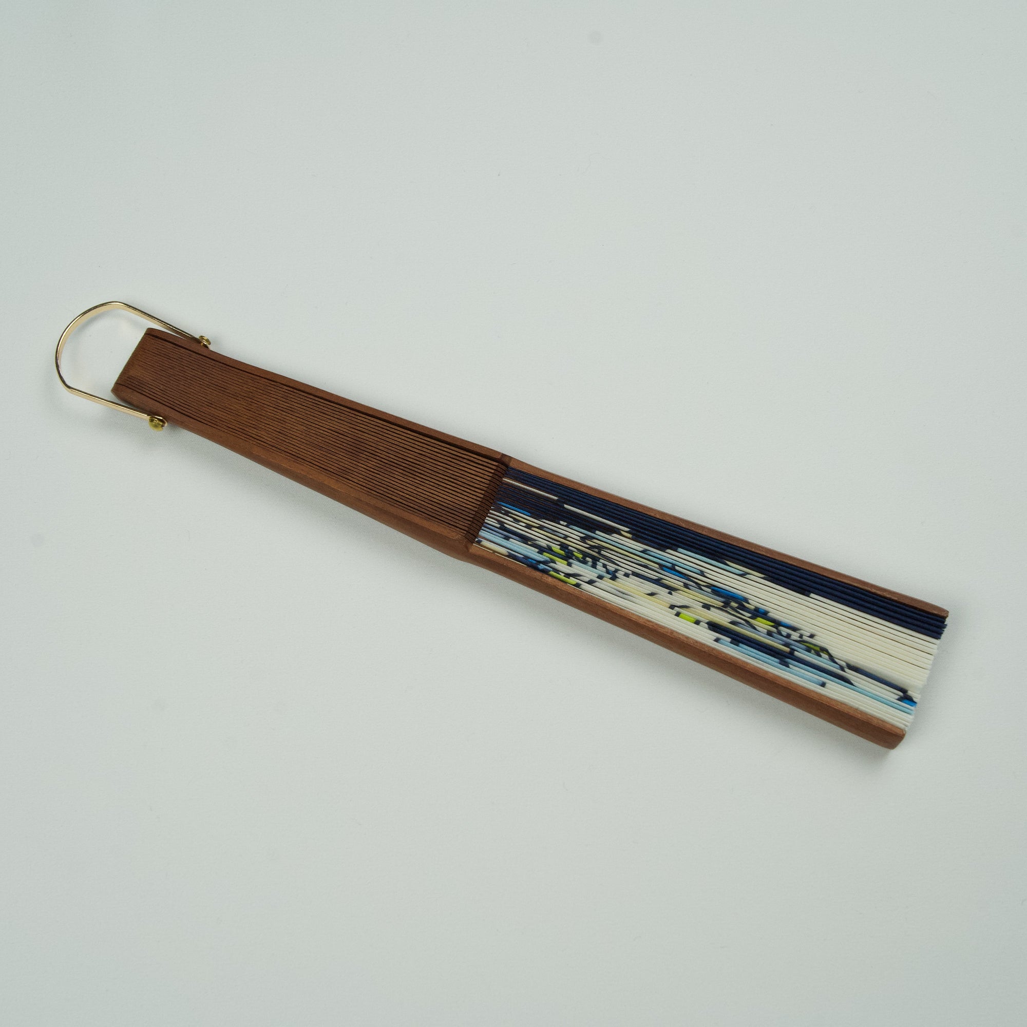 Handbeschilderde zijden waaier van Ottimare in blauw met de afbeelding van twee zusjes. Het op deze afbeelding dichtgeklapte frame is van Kotibé hout en artisanaal opgespannen.