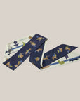 Extra lange tangram sjaal van Ottimare met een dusk blauwe en een ivoor kleurige achtergrond. De figuurtjes zijn in grijs, groen, camel en blauwe tinten.