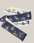 Extra lange tangram sjaal van Ottimare met een dusk blauwe en een ivoor kleurige achtergrond. De tangram figuurtjes zijn in grijs, groen, camel en blauwe tinten.