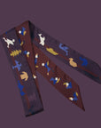Afbeelding van Ottimare's extra lange Tangram sjaal met twee verschillende kanten. De achtergrond is bordeaux en aan de andere kant Aubergine met een bordeaux streep. De figuren zijn in verschillende kleuren blauwe, camel, goud en ivoor. Speels en combineert met heel veel tops!