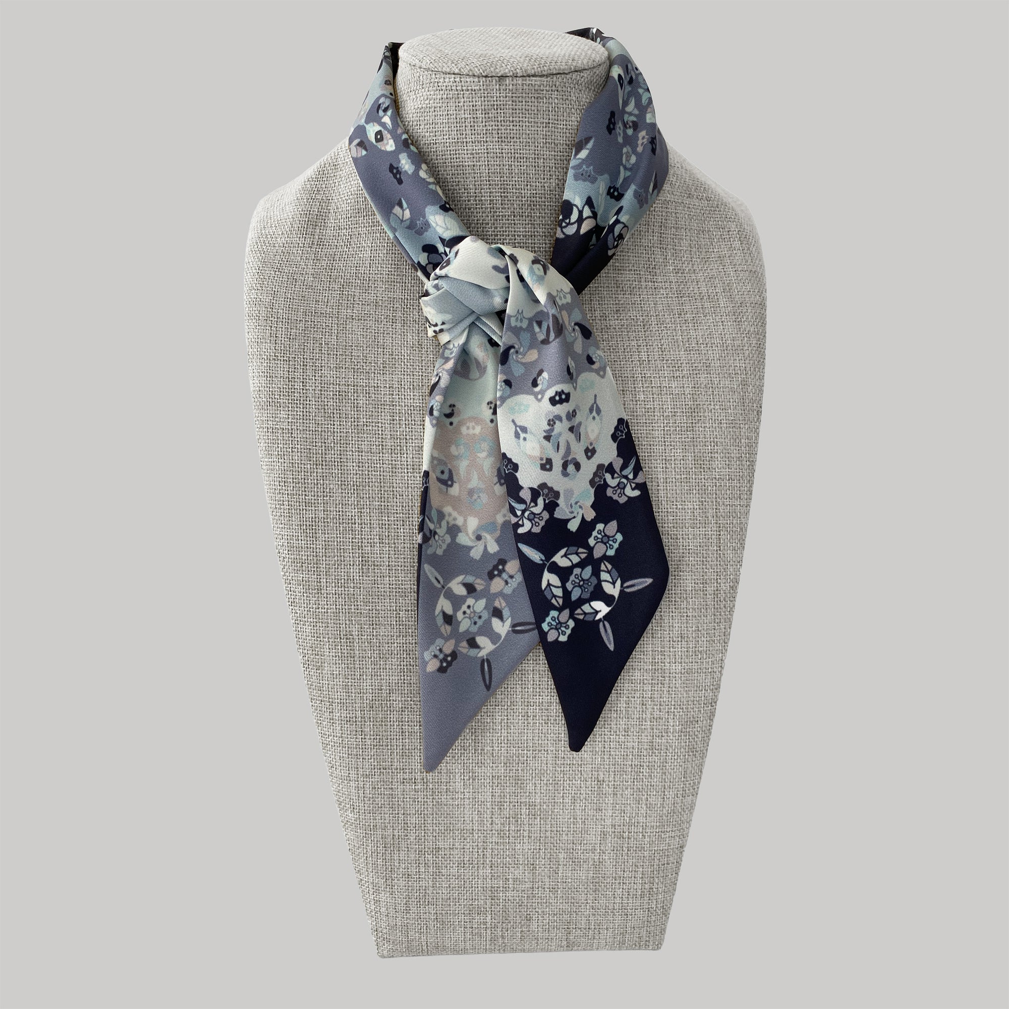 Ottimare twilly sjaaltje op een pop. De damessjaal heeft grijze en zwarte jasmijn bloemen als print en is met de hand gemaakt van duurzame eco twill kunst zijde in Nederland. 
