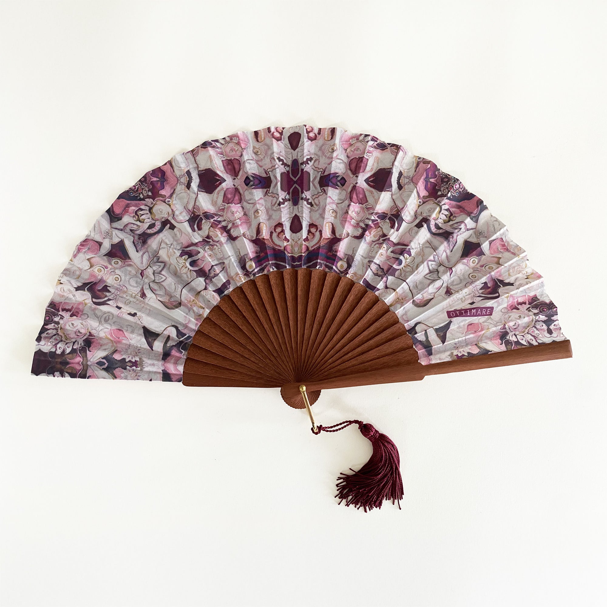 Ottimare waaier met Thangka danser print op duurzame kunst zijde in roze en bordeaux op een houten frame dat is handgemaakt in Spanje. Het frame is van Kotibé hout. Aan de goudkleurige ring kan een klosje of draagkoord worden bevestigd.