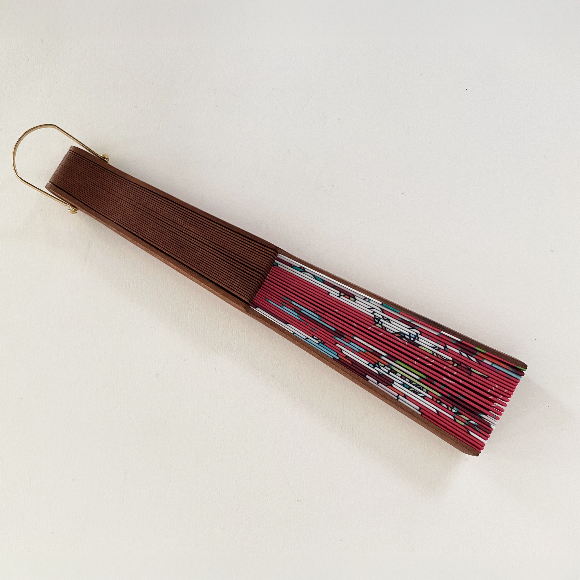 Opgevouwen waaier van Ottimare in koraal rood  met groene accenten. Het houten frame is handgemaakt in Spanje en heeft een goudkleurige ring. De housoort is Kotibé.