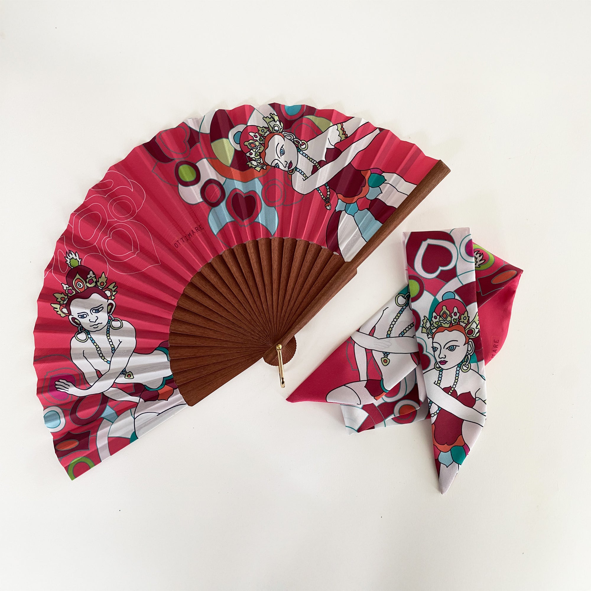 Waaier en bijpassende twilly sjaal van Ottimare met twee Thangka dansers tegen een koraal rode achtergrond met groene accenten. Het houten frame is handgemaakt in Spanje en heeft een goudkleurige ring.