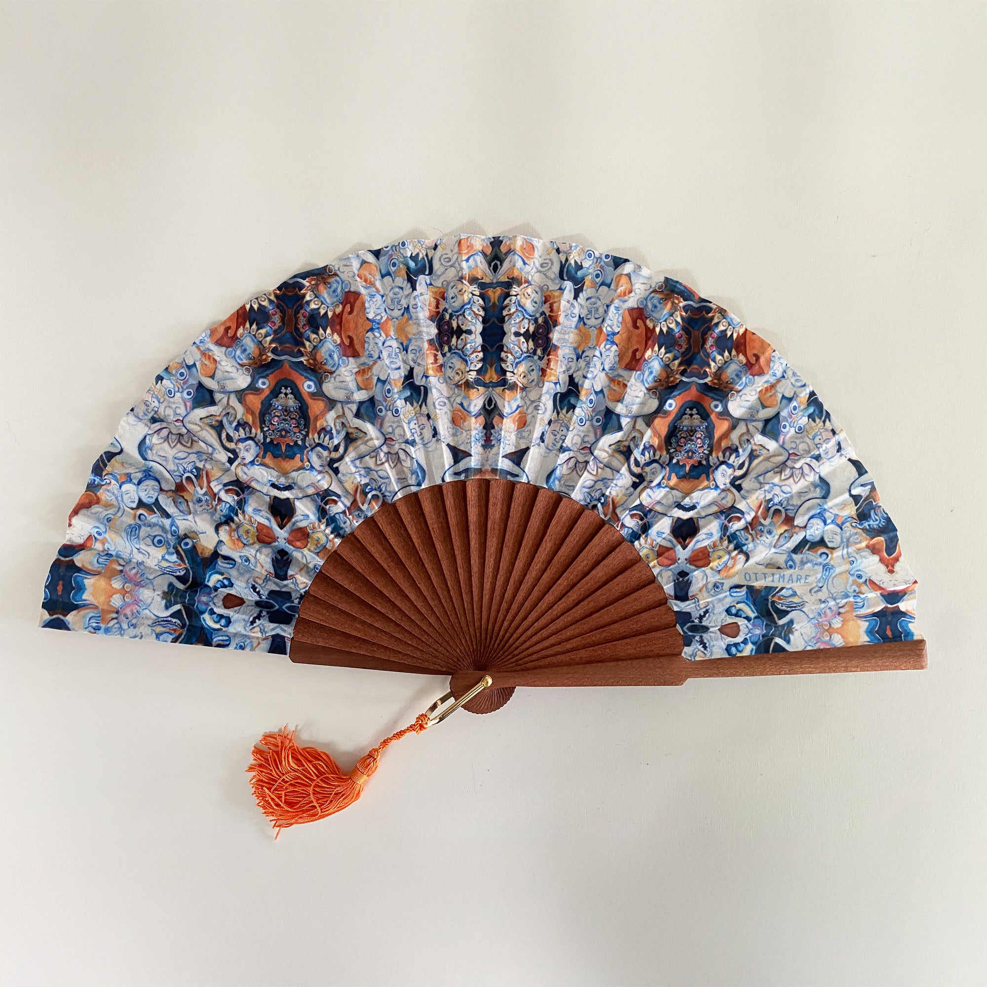 Elegante waaier van Ottimare met print op duurzame kunst zijde met Thangka dansers in donker blauw en sienna oranje. Het frame is van Kotibé hout en handgemaakt in Spanje.